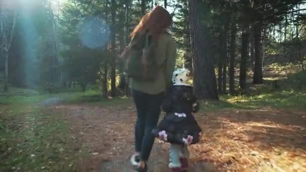 Madre e hija felices están caminando a lo largo del camino forestal. Madre e hija caminando en el bosque de otoño. vomitar las hojas amarillas de otoño . — Vídeos de Stock