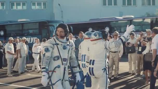 Três cosmonautas reais vivos vão ao foguete, dizem adeus a uma multidão de pessoas, acenam com as mãos. Vestida com um fato espacial. Lançamento do foguete espacial Soyuz FG MS-05 . — Vídeo de Stock