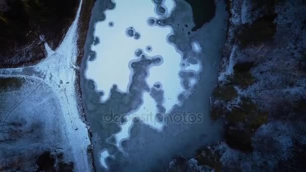 Vuelo en un dron sobre un lago congelado. Círculos de hielo en el agua. Lago en invierno en un bosque o parque, entre árboles . — Vídeos de Stock