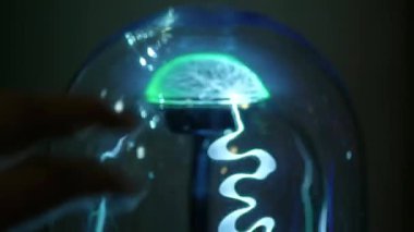 Yeşil soyut elektrik ışık bir cam şişeye. Bir plazma topu gibi. Adamın parmaklarını yıldırım dokunur. İletim elektrik enerjisi havada, elektrik kablosuz iletim