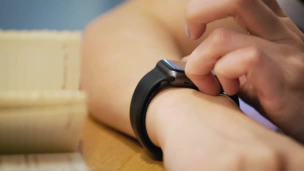 Faire divers gestes avec un doigt sur un écran tactile d'un appareil portable de montre intelligente. la fille est assise dans le café, utilise une horloge intelligente — Video