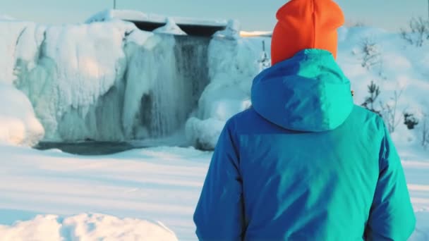 A young girl takes a photo of a frozen waterfall, takes pictures on a smartphone. Water flows, ice floes and icicles, a winter Christmas fairy tale — Stock Video