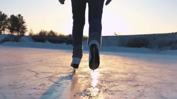 Nahaufnahme, Tiefblick: Glückliche Frau, die an einem magischen Heiligabend bei goldenem Sonnenuntergang auf einem zugefrorenen Teich im örtlichen Park schnell Eisklettern kann. Menschen auf Schlittschuhen genießen Winteraktivitäten in der Natur, Spaß haben — Stockvideo