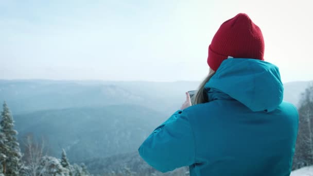 Mladá dívka turistické dělá foto na smartphone v zimě. Fotografie zasněžené vrcholky hor — Stock video