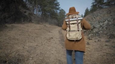 Etkin sağlıklı hipster teen ormanda hiking. Genç kız Gezgin ormanda yürür. Bir şapka ve bir seyahat etmek sırt çantası konur. 120 fps ağır çekim