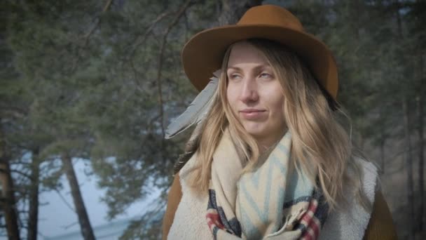 Jeune fille voyageuse regarde le soleil. Coucher de soleil ou aube. Un chapeau et un sac à dos sont mis. Dans le contexte d'une pinède et d'une rivière gelée en hiver — Video