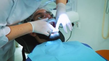 Dişçi ofiste iş başında. Kadın doktor diş ve çene erkek hastanın inceliyor..
