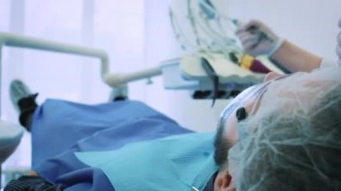 Dişçi ofiste iş başında. Kadın doktor diş ve çene erkek hastanın inceliyor..