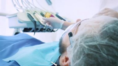 Dişçi ofiste iş başında. Kadın doktor diş ve çene erkek hastanın inceliyor..