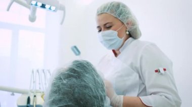 Kadın dişçi ofisinde. Bir kadın doktor diş hekimi çene ve diş erkek hastanın üzerinde çalışıyor. Kamera, Doktor ortodontist portresi bakar.