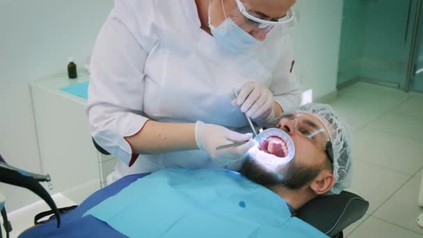 Dentista trabajando en la oficina. Una doctora examina los dientes y las mandíbulas de un paciente masculino .. — Vídeos de Stock
