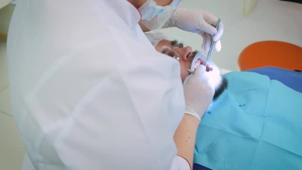 Zubař v práci v kanceláři. Ženský lékař zkoumá zuby a čelisti pacienta mužského pohlaví.. — Stock video