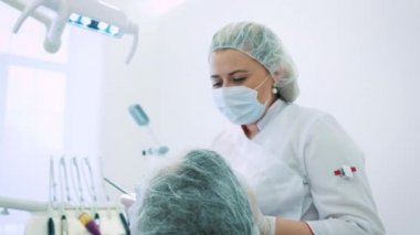 Kadın dişçi ofisinde. Bir kadın doktor diş hekimi çene ve diş erkek hastanın üzerinde çalışıyor. Kamera, Doktor ortodontist portresi bakar.