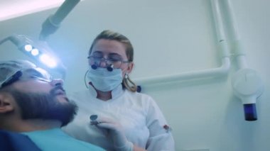 Dişçi ofiste iş başında. Kadın doktor diş ve çene erkek hastanın inceliyor..