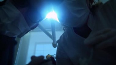 bir dişçi maskeli iki doktor olduğunu gülen, bir ağız ayna ve kanca Holding, döner ışık, diş lamba açık, ışıklar içine bir hasta ağız, ayakta üzerine bir kameraya, seyir hasta, çalışıyor