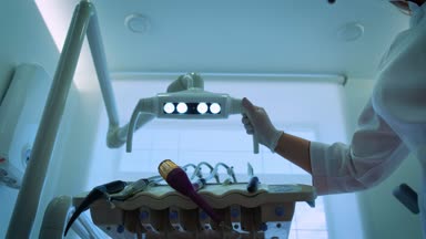 bir dişçi maskeli iki doktor olduğunu gülen, bir ağız ayna ve kanca Holding, döner ışık, diş lamba açık, ışıklar içine bir hasta ağız, ayakta üzerine bir kameraya, seyir hasta, çalışıyor