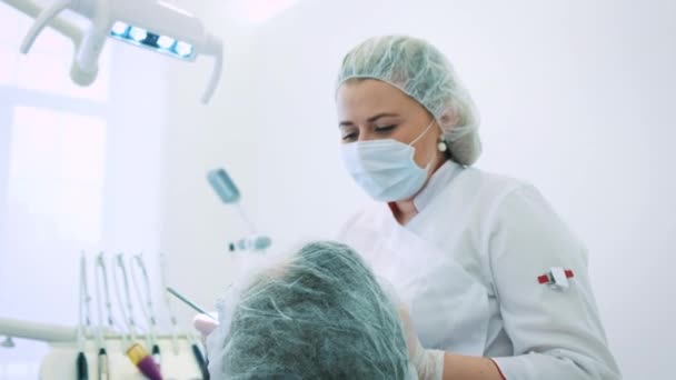 Une femme dentiste au bureau. Une femme médecin dentiste travaille sur la mâchoire et les dents d'un patient masculin. Regarde la caméra, portrait du médecin orthodontiste . — Video