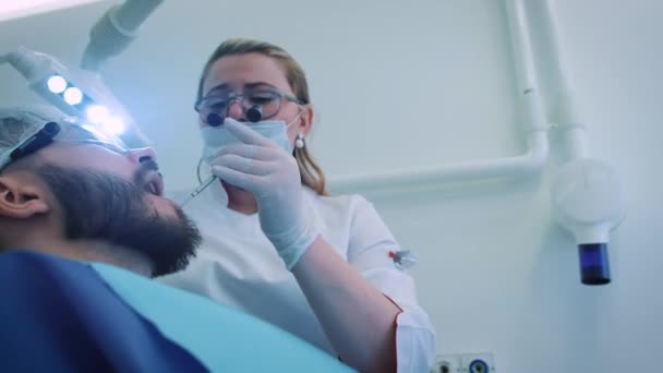 Tandarts op het werk in het kantoor. Een vrouwelijke arts onderzoekt de tanden en de kaken van een mannelijke patiënt.. — Stockvideo