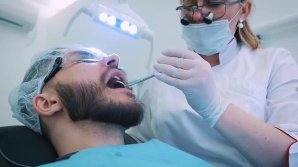 Dentista trabajando en la oficina. Una doctora examina los dientes y las mandíbulas de un paciente masculino .. — Vídeo de stock