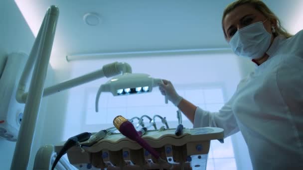 Due medici del dentista in maschera è sorridente, tenendo in mano uno specchio bocca e gancio, accende la luce della lampada dentale, si accende in una bocca pazienti, in piedi su un paziente, Guardando la fotocamera, cercando — Video Stock