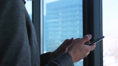 Sakallı genç başarılı işadamı bir pencere arka planda şehir manzarasına sahip bir smartphone üzerinde bir çağrı yapar. Yüksek işletme binası. Office loft tarzı.