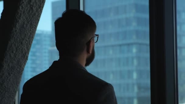 Junger erfolgreicher Geschäftsmann, der aus dem Fenster auf die Innenstadt blickt. Hohes Geschäftshaus. Büro im Loft-Stil — Stockvideo