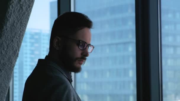 Jovem empresário de sucesso fazendo selfie no fundo de uma janela com vista para o centro da cidade. Edifício de negócios. Escritório em estilo loft — Vídeo de Stock