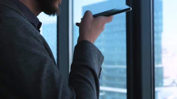 El hombre de negocios sonríe después de enviar un mensaje de voz. Joven moderno a la moda con un hombre de negocios barba escribiendo un mensaje de voz en un smtrmfon. Situado en una oficina moderna . — Vídeos de Stock