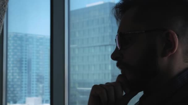 Young successful businessman with a beard thinking in the background of a window overlooking the downtown. High business building. Office in loft style — Stock Video