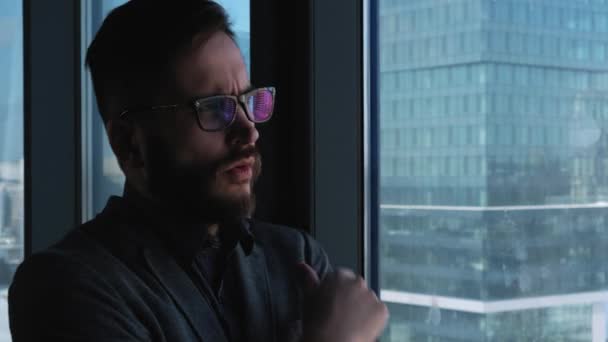Young successful businessman with a beard thinking in the background of a window overlooking the downtown. High business building. Office in loft style — Stock Video