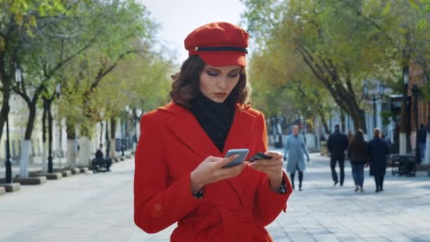 A young girl stands on a city street. Holding a smartphone and a bank card. Makes electronic payment by credit card via smartphone. Online shopping — Stock Video