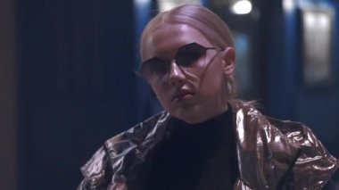 Geceleri sokakta poz veren güzel bir genç kız. Parlak bir ceket ve güneş gözlüğü takıyordu. Şehirde fotoekonomik durgunluk