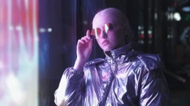 Genç bir kız model neon ışıklarda duruyor. Milenyum 'un hüzünlü, güzel ve alışılmadık saç stili olan kızı geceleri şehrin parıldayan neon ışıkları altında. Kızın kameraya baktığı gece hayatı atmosferi.