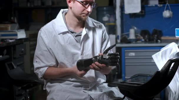 Bir mühendis elektronik biyonik protez kolu test ediyor. Mekanik bir kolun plastik parmaklarını hareket ettiriyor. Protezde modern teknolojiler. Bir bilim adamının elinde sibernetik bir el — Stok video