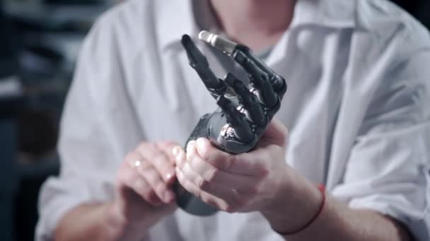 A scientist engineer is testing an electronic bionic prosthetic arm. He moves the plastic fingers of a mechanical arm. Modern technologies in prosthetics. Cybernetic hand in the hand of a scientist — Stock Video