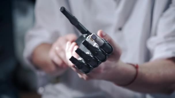 A scientist engineer is testing an electronic bionic prosthetic arm. He moves the plastic fingers of a mechanical arm. Modern technologies in prosthetics. Cybernetic hand in the hand of a scientist — ストック動画