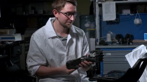 A scientist engineer is testing an electronic bionic prosthetic arm. He moves the plastic fingers of a mechanical arm. Modern technologies in prosthetics. Cybernetic hand in the hand of a scientist — Stock Video