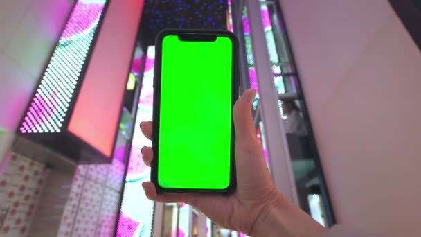 Una mano tiene uno smartphone con uno schermo verde sullo sfondo delle luci al neon di un centro commerciale a Las Vegas. Shopping serale alla moda — Video Stock