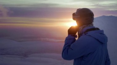 Bir kayakçı ya da snowboardcu bir dağda durup gün batımını izliyor. Mavi ceket ve kayak kaskı giymişti. Rusya 'nın kuzeyinde karla kaplı kış dağları, Khibiny