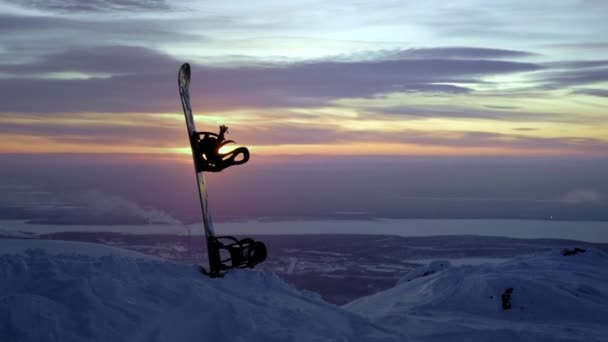 Snowboard stoi w śniegu. Utknął w zaspie śnieżnej na tle zachodu słońca. Zimowe góry pokryte śniegiem na północy Rosji, Khibiny. Krajobraz wieczorny poza kołem podbiegunowym — Wideo stockowe