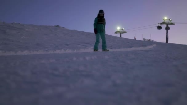 Snowboardista sklouzne ze svahu na snowboardu. Večerní lyžování — Stock video