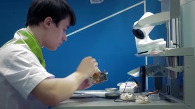 Diş hekimi çenesine takma diş takıyor. Dişçi elinde bir çene implantı tutuyor ve malzemeyi aletlerle uyguluyor. Modern dişçilik teknolojileri. Yakın plan, 4k..