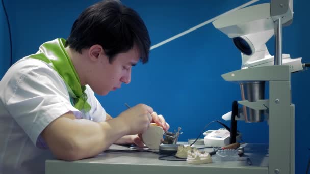 A fogorvos műfogsort készít az állkapcsára. A fogorvos állkapocs implantátumot tart a kezében, és szerszámokkal alkalmazza az anyagot. Modern technológiák a fogászatban. Közelkép, 4k. — Stock videók