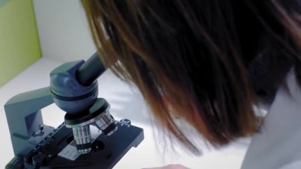 Jeune fille scientifique qui regarde au microscope. Elle étudie les échantillons. Un jeune scientifique mène des recherches scientifiques. Elle fait des recherches sur un virus, cherche un remède pour un vaccin épidémique — Video