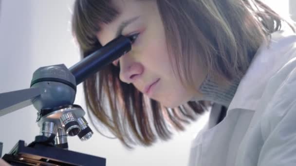 Молода дівчина вчений дивиться через мікроскоп. Вона вивчає зразки. Молодий вчений проводить наукові дослідження. Вона досліджує вірус, шукає ліки від епідемічної вакцини — стокове відео