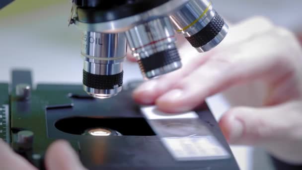 Um cientista olha através de um microscópio. Muda de amostra. Realiza trabalhos de investigação científica. Está a pesquisar um vírus, à procura de uma cura para uma vacina epidémica. — Vídeo de Stock