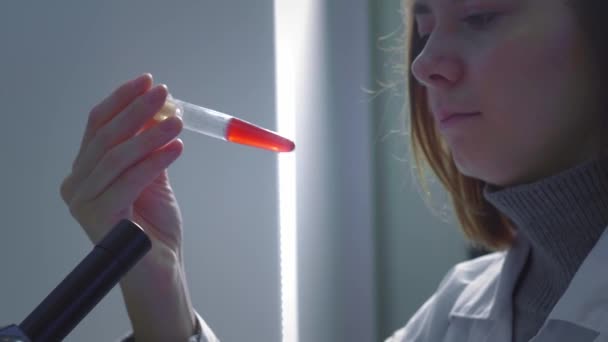 若い女の子科学者は、血液とテストチューブを検討します.彼女はサンプルを研究してる若い科学者が科学研究を行う。流行性ワクチンの治療法を探してウイルスを研究しています — ストック動画