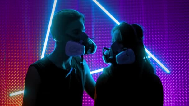Young couple in the neon lights of the club. Concept of dubstep or punk style. Wearing a gas mask from dirty air. Protected in a public place from the Chinese coronavirus. — Stock Video