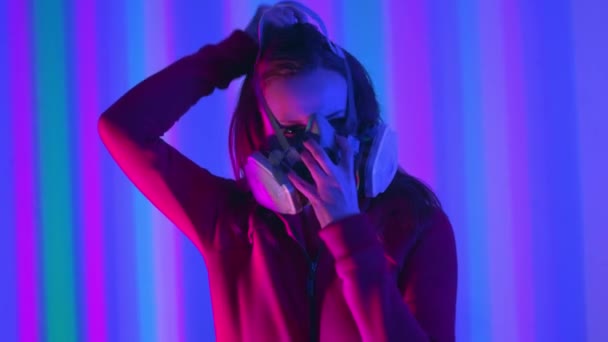 Young girl model in the neon lights of the club. Concept of dubstep or punk style. Wearing a gas mask from dirty air. Protected in a public place from the Chinese coronavirus. — Stock Footage Young girl model in the neon lights of the club. Concept of dubstep or punk style. Wearing a gas mask from dirty air. Protected in a public place from the Chinese coronavirus. — Stock Video