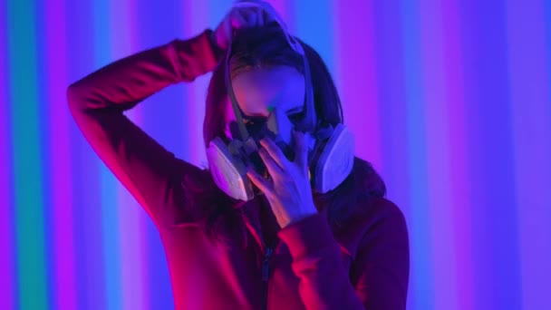 Young girl model in the neon lights of the club. Concept of dubstep or punk style. Wearing a gas mask from dirty air. Protected in a public place from the Chinese coronavirus. — Stock Video